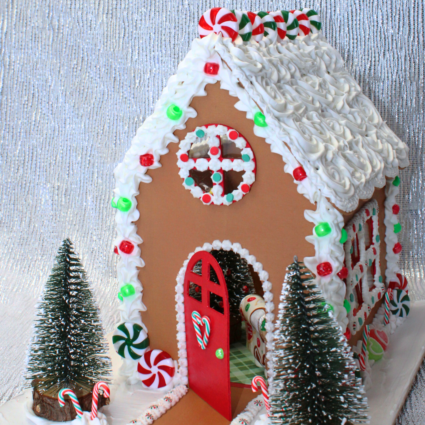 Decorative cardboard gingerbread house with plastic candy decorations on a shiny silver background. 