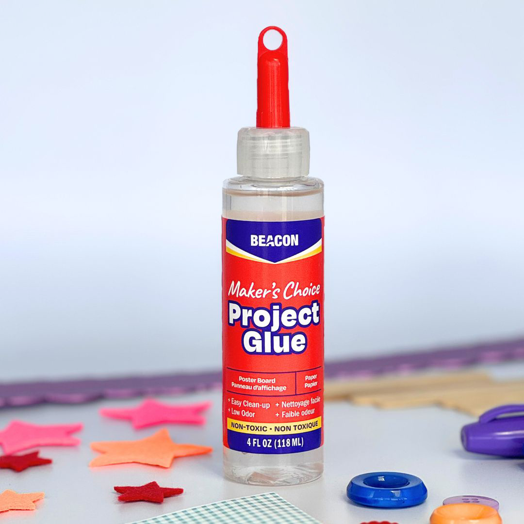 A bottle of Beacon Maker's Choice Project Glue with a red cap, set on a white surface with colorful star-shaped felt cutouts, buttons, and paper in the background.
