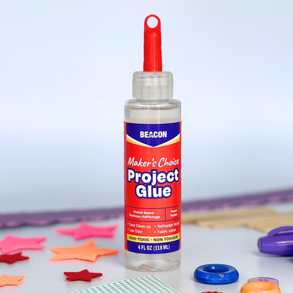 A bottle of Beacon Maker's Choice Project Glue with a red cap, set on a white surface with colorful star-shaped felt cutouts, buttons, and paper in the background.