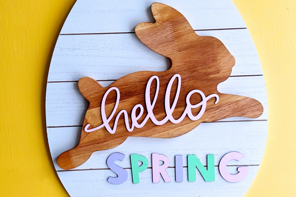 Wooden sign in the shape of an egg. A wooden rabbit and letters are glued to the sign saying "hello spring"